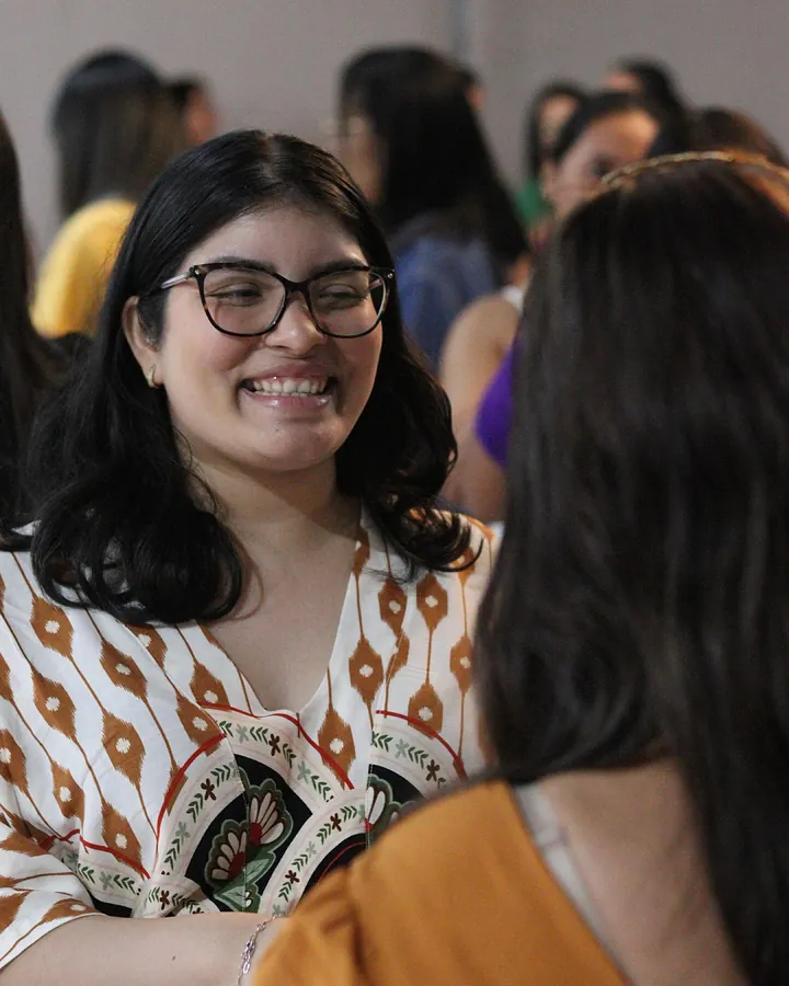 Mulher sorrindo de óculos durante um encontro do TPM, conversando com outras mulheres